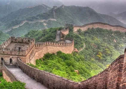 Die Chinesische Mauer schlängelt sich bei Sonnenuntergang durch die grünen Berge nahe Peking.
